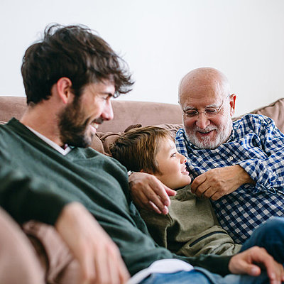 Großvater, Vater und Sohn sitzen auf einer Couch und lachen miteinander