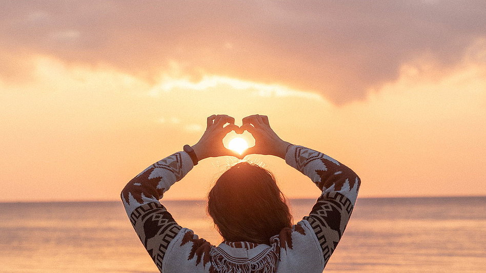 Eine Frau am Strand mit hochgehaltenen Händen, die ein Herz formen