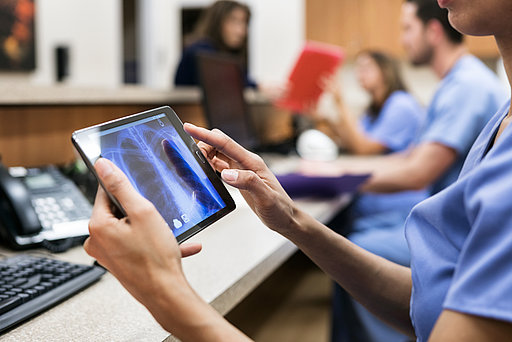 Eine medizinische Fachkraft mit einem Tablet, auf dem eine Röntgenaufnahme zu sehen ist