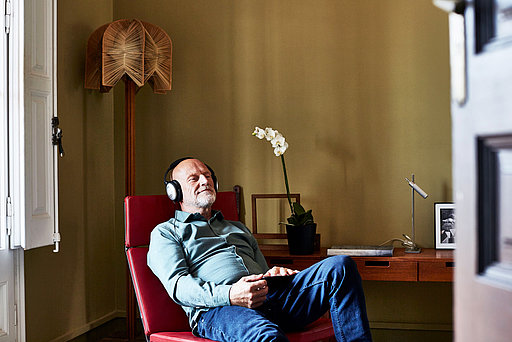 Älterer Mann mit Kopfhörern sitzt auf Sessel 
