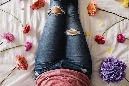 Eine Frau liegt auf dem Bett umringt von Blumen