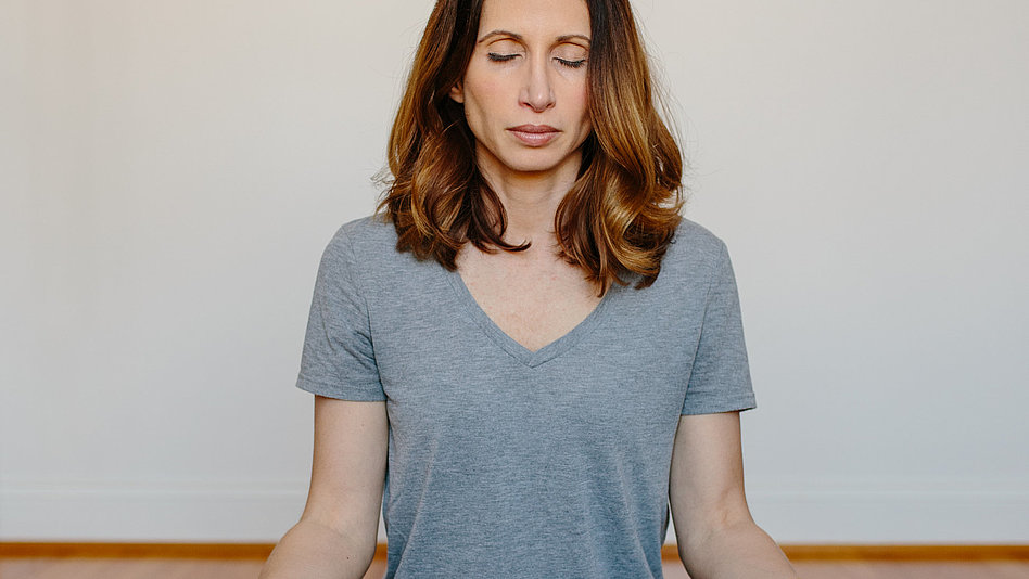 Eine Frau sitzt mit geschlossenen Augen im Yogasitz auf der Matte 