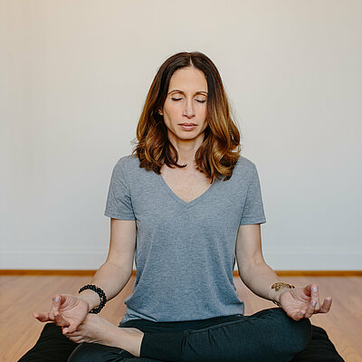Eine Frau sitzt mit geschlossenen Augen im Yogasitz auf der Matte 