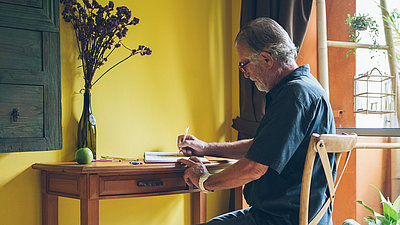Ein Mann sitzt am Tisch und schreibt in ein Notizbuch
