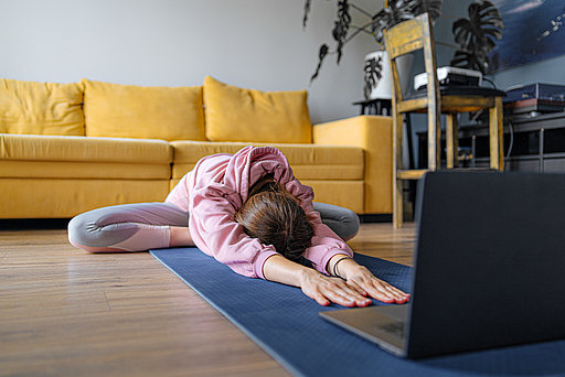 Eine Frau führt Dehnübungen auf einer Yoga- matte zu Hause aus