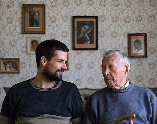 Ein junger und ein alter Mann sitzen nebeneinander und blicken sich gegenseitig an