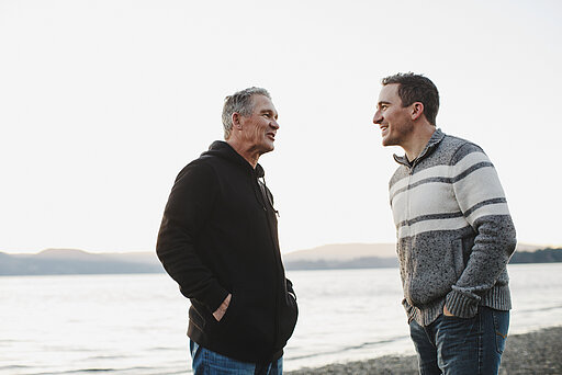 Zwei Männer unterschiedlicher Generationen stehen sich einander am Ufer eines Gewässers gegenüber