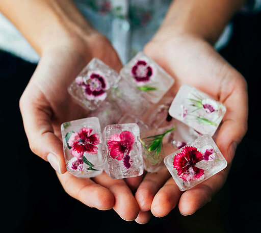 In Kunststoff konservierte Blüten liegen in zwei Händen.