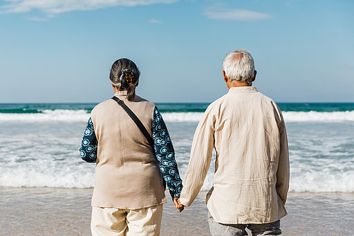 Ein Paar steht Hand in Hand am Strand und blickt auf das Meer