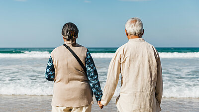 Ein Paar steht Hand in Hand am Strand und blickt auf das Meer