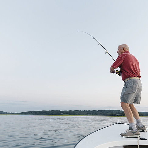 Älterer Mann steht auf einem Boot und angelt 
