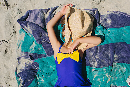 Mädchen im blauen Badeanzug liegt in der Sonne mit Strohhut auf dem Gesicht 