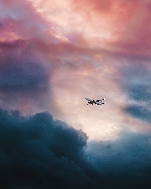 Flugzeug vor einem Wolkenpanorama in pink-grauen Farbtönen.