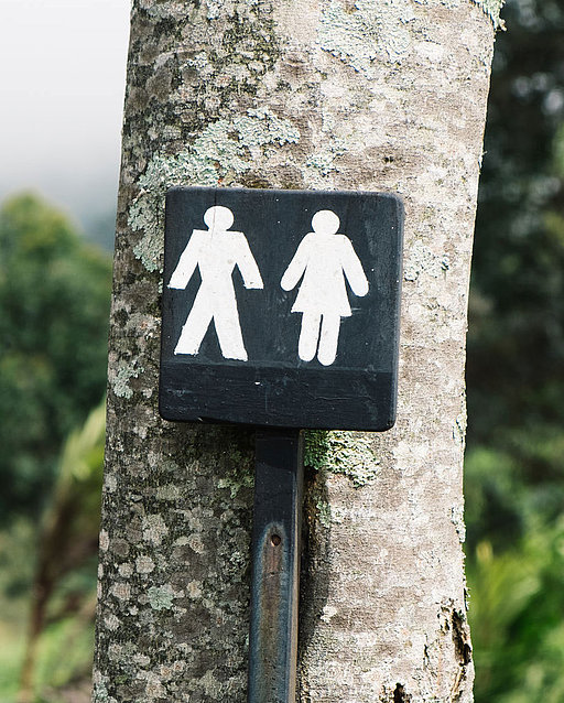 Schild mit Mann- und Frau-Symbol vor einem Baum