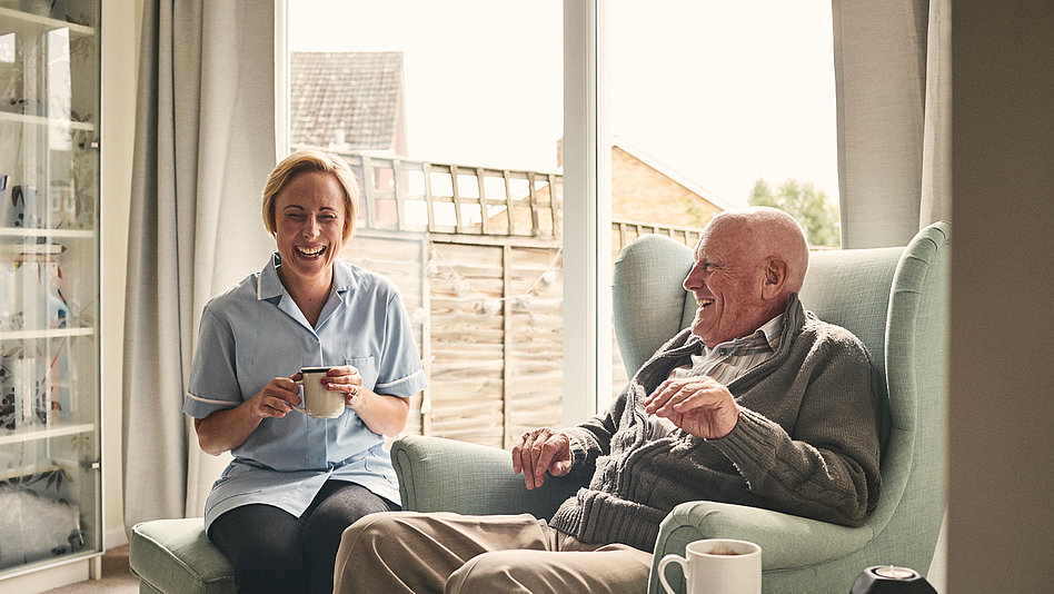 Krankenpflegerin und älterer Mann trinken einen Tee.