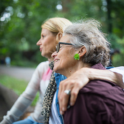 Zwei Frauen sitzen gemeinsam im Park und legen die Arme umeinander