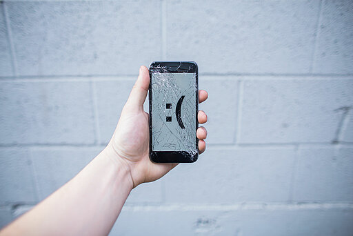 Handy mit kaputtem Display, das einen traurigen Smiley zeigt.