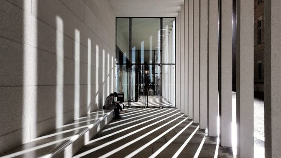 Sonnenstrahlen treten durch Betonsäulen vor einem Gebäude