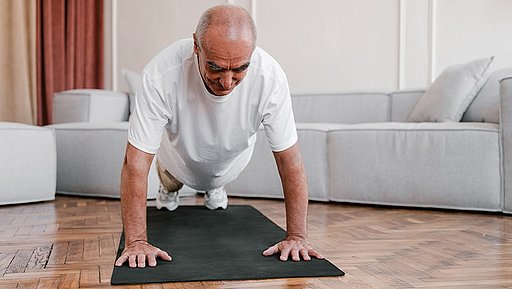 Älterer Mann macht Liegestütze auf einer Trainingsmatte im Wohnzimmer