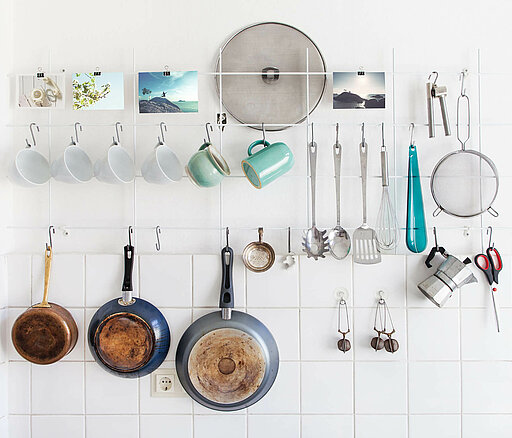 Küchenutensilien an der Wand: Tassen, Pfannen, Kochbesteck, Schere, Teesieb und Kaffeekocher