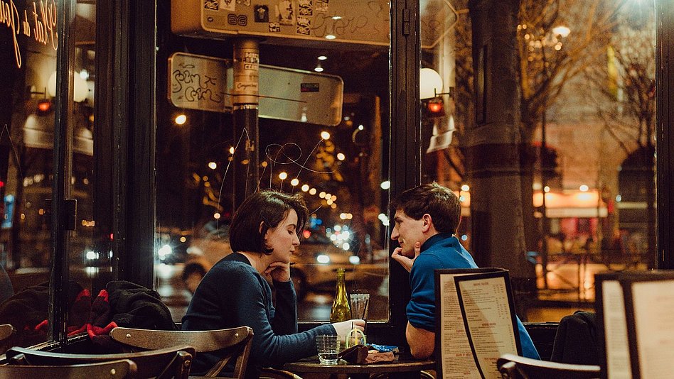 Mann und Frau sitzen bei gedämmtem Licht in einer Bar am Fenster.