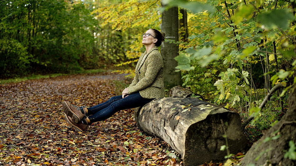 Frau sitzt auf Baumstamm im Wald