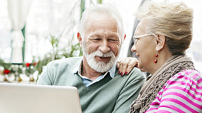 Älteres Paar vor einem Laptop im fröhlichen Gespräch