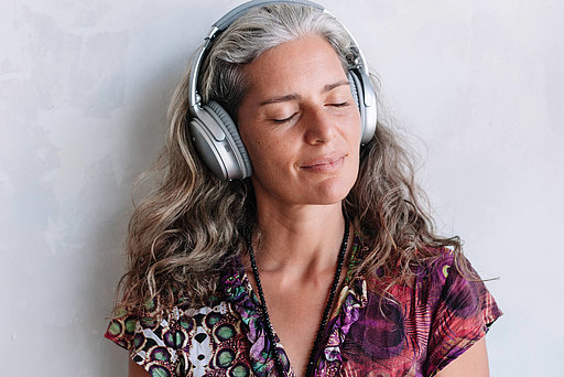 Frau mittleren Alters hört mit Kopfhörer Musik und hat die Augen geschlossen.