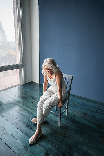 Ältere Frau sitzt allein in einem Zimmer auf dem Stuhl