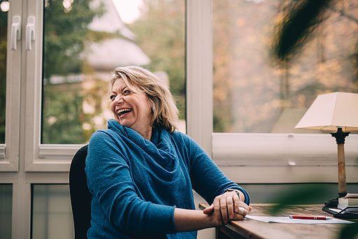 Psychoonkologin Dr. phil. Katrin Reuter sitzt am Schreibtisch und lacht ausgelassen über ihre Schulter hinweg