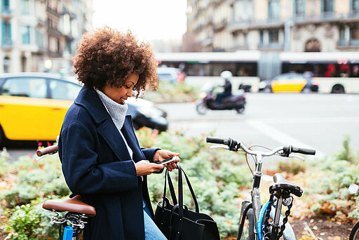 Frau auf Fahrrad blickt lächelnd auf Smartphone