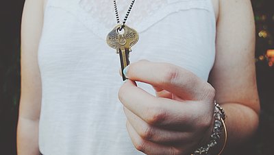 Eine Hand hält einen goldenen Schlüssel, der an einer Halskette hängt.