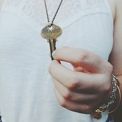 Eine Hand hält einen goldenen Schlüssel, der an einer Halskette hängt.