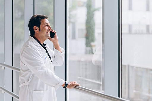 Ein Arzt steht mit einem Telefon am Ohr in einem lichtdurchfluteten Krankenhausflur