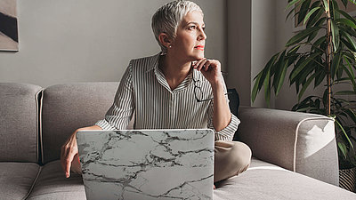 Eine Frau sitzt auf einem Sofa im Schneidersitz vor einem Notebook